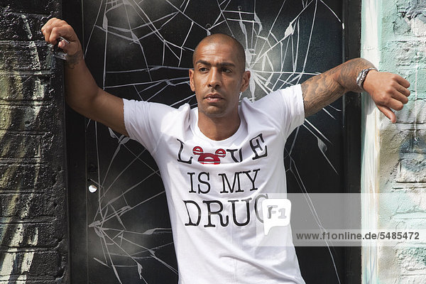 Dunkelhäutiger Brite mit Tätowierungen und T-shirt mit der Aussage Love is my drug  Porträt  East End  London  England  Großbritannien  Europa