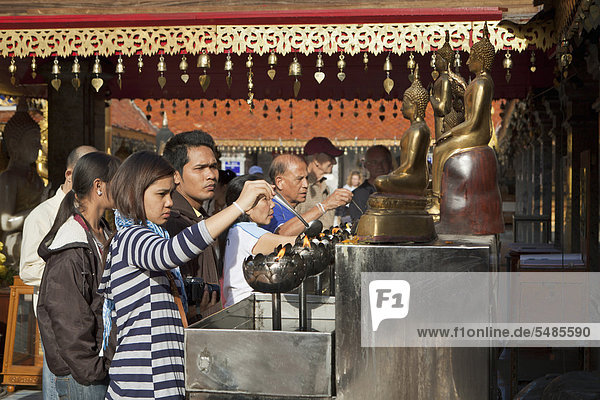 People pouring oil to burn in lotus-shaped metal bowls  Wat Phra That Doi Suthep  Chiang Mai  Thailand  Asia