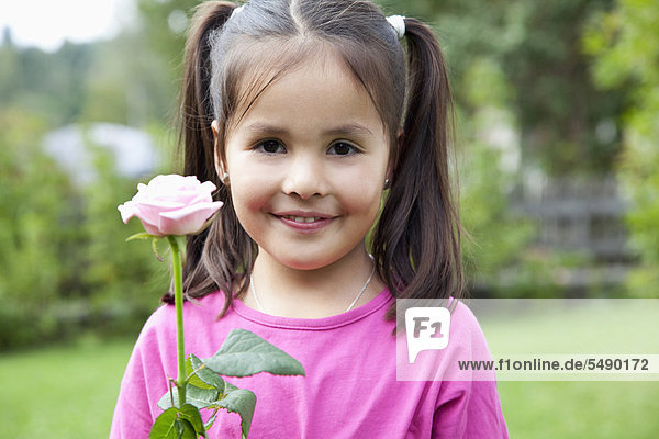 Mädchen hält Blume im Garten  lächelnd  Portrait