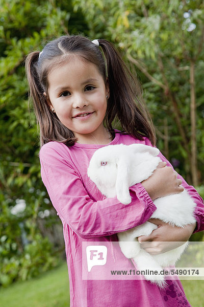 Mädchen hält Kaninchen im Garten  lächelnd  Portrait