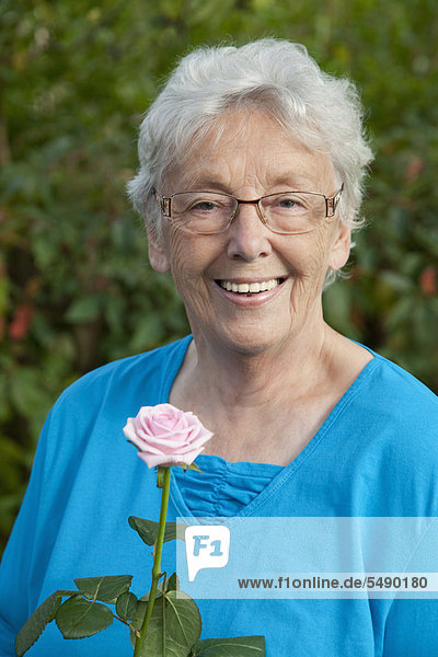 Senior woman with rose in garden  smiling  portrait