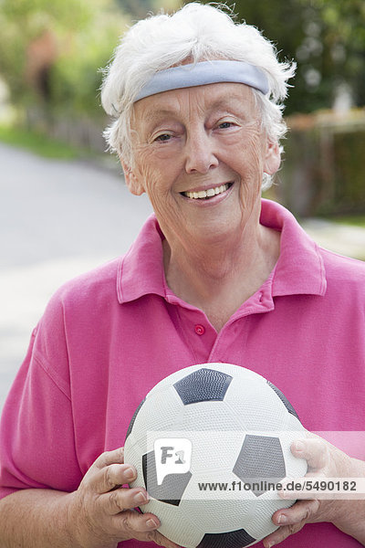 Senior woman holding soccer ball  smiling  portrait