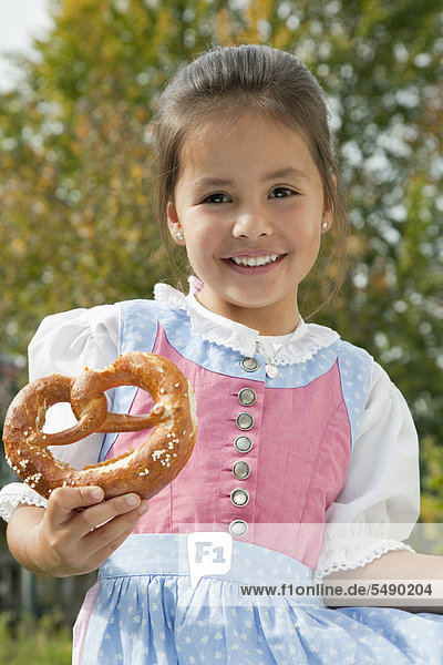 Girl holding pretzel in garden  smiling  portrait