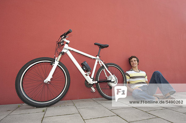 Junger Mann neben dem Fahrrad sitzend  lächelnd