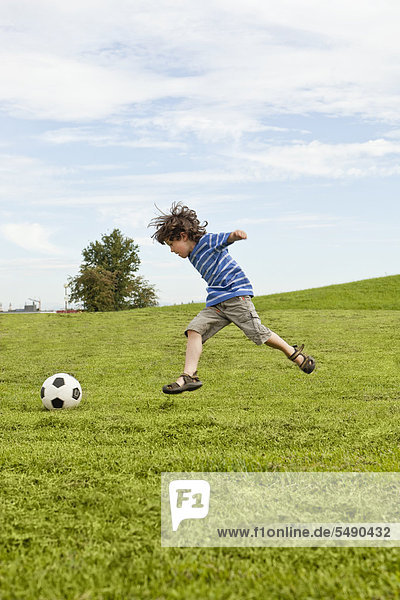 Junge spielt mit Fußball im Park.