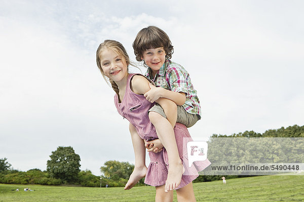 Girl giving piggy back ride to boy in park  smiling  portrait