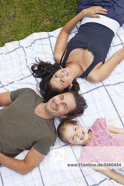 Deutschland  Bayern  Familie auf Decke im Park liegend  lächelnd