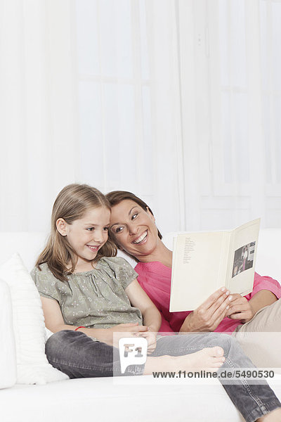 Deutschland  München  Mutter und Tochter lesen Buch  lächelnd