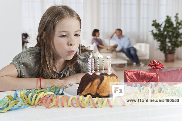 Mädchen bläst Kerzen von Geburtstagskuchen  Eltern im Hintergrund