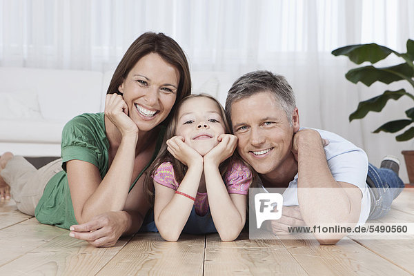 Germany  Munich  Parents and daughter lying on floor  smiling  portrait