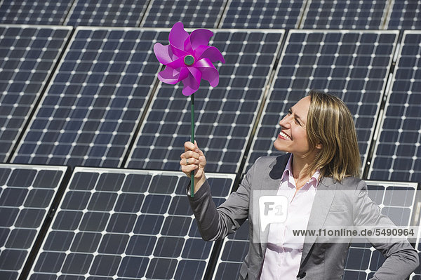 Frau hält Papierwindmühle gegen Sonnenkollektoren  lächelnd