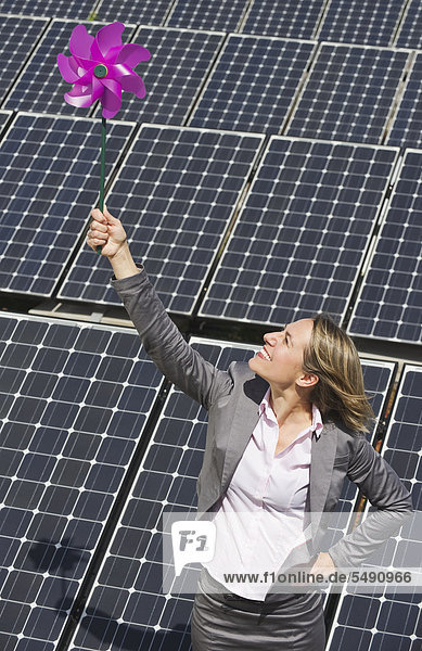 Woman holding paper windmill against solar panels  smiling