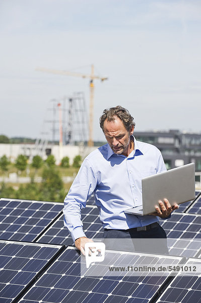 Erwachsener Mann mit Laptop in Solaranlage