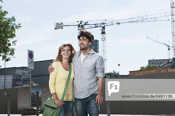 Deutschland  Köln  Junges Paar stehend mit Baustelle im Hintergrund  lächelnd