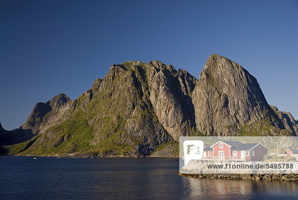 Typical red rorbuer huts  rorbu  at the coast of the Norwegian Sea  mountains at back  Hamn¯y  island of Moskenes¯y  Moskenesoy  Lofoten archipelago  Nordland  Norway  Europe