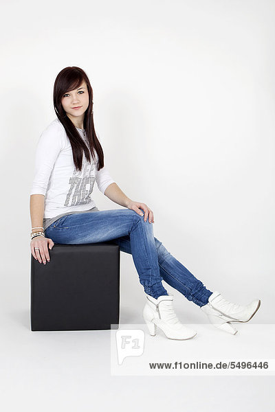 Young woman wearing a white top and jeans posing on a black cube seat