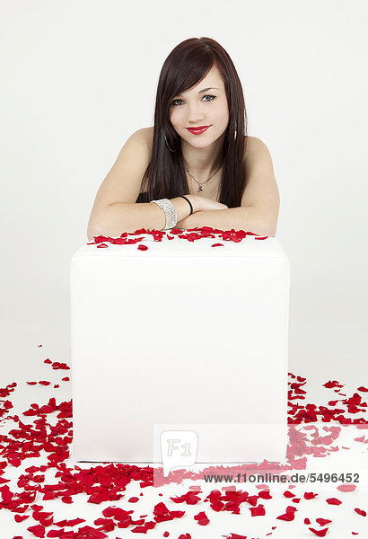 Young woman leaning against a white cube seat with rose petals