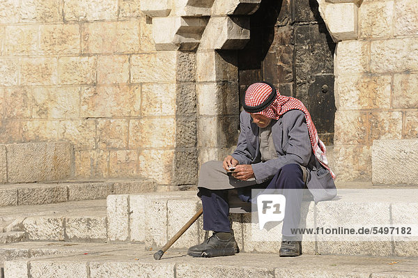 Einsam sitzender Palästinenser mit Kufiya oder Kafiya oder Kefije auf den Stufen des Damaskustores  Altstadt  Jerusalem  Israel  Vorderasien