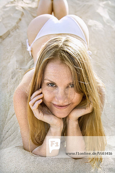 Porträt im Sand Bikini tragen ziemlich Rothaarige Frau liegen.
