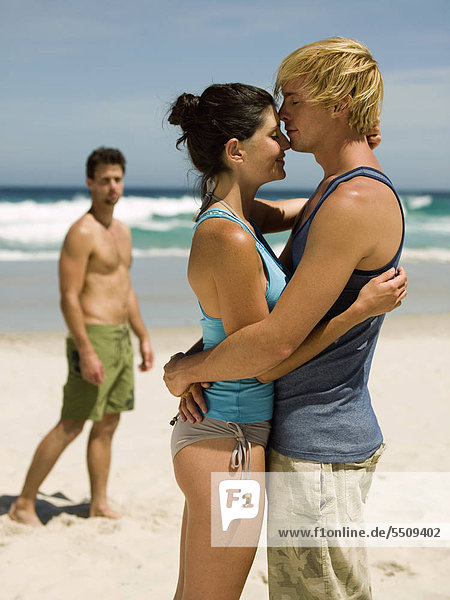 Paar am Strand Mann im Hintergrund