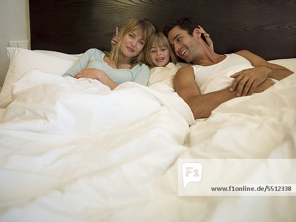 Eltern und Tochter faulenzen im Bett