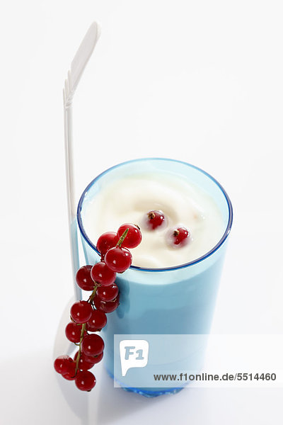 Blauer Becher und weißer Kunststofflöffel mit Joghurt und Johannisbeeren