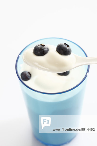 Blauer Becher und weißer Kunststofflöffel mit Joghurt und Blaubeeren