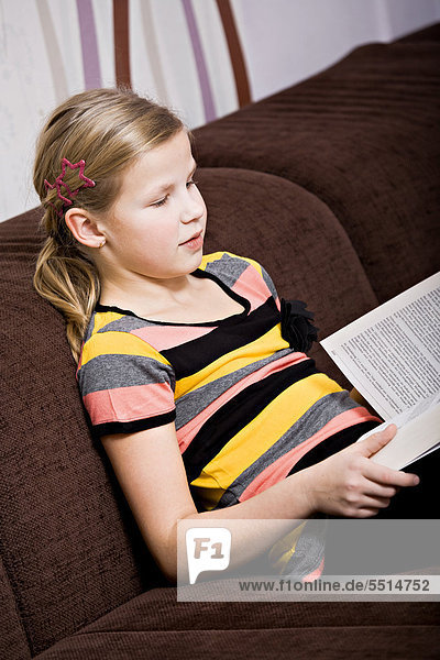 11-jähriges Mädchen liest Buch auf Sofa