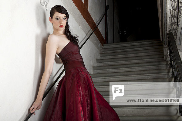 Junge Frau mit rotem Kleid steht auf Steintreppe in Treppenhaus