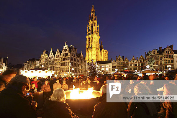 Menschen trinken Glühwein an einem großen Gasflammenlagerfeuer auf dem Weihnachtsmarkt am Rathaus auf dem Grote Markt  umsäumt von alten Gildehäusern  Altstadt  Antwerpen  Flandern  Belgien  Europa
