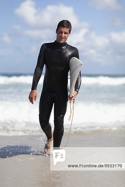 Teenage surfer carrying board on beach