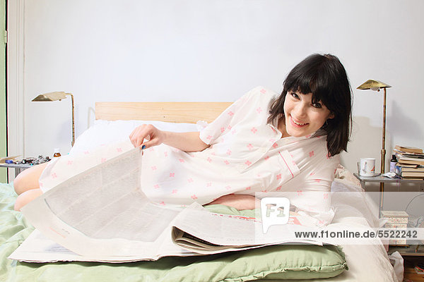 Woman reading newspaper in bed