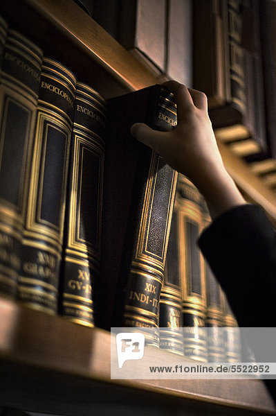 Hand zieht Buch aus Bücherregal