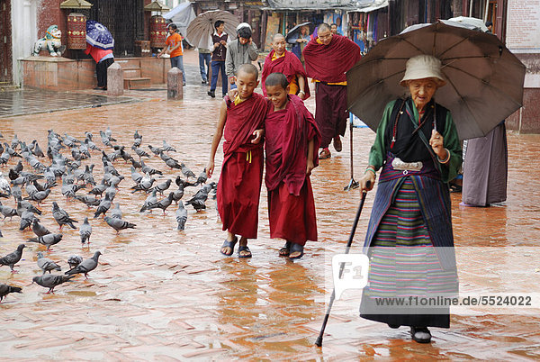 Pilgerin mit Schirm und Mönche umrundet bei Regen Stupa von Bodnath  Kathmandu  Nepal  Asien