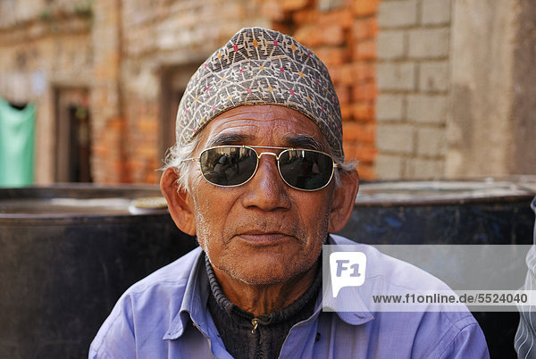 Mann mit Sonnenbrille und traditioneller Kopfbedeckung  Porträt  Bhaktapur  Kathmandu Tal  Nepal  Asien