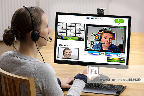 Junge Frau sitzt am Computer und telefoniert über das Internet  per Webcam wird das Livebild beider Teilnehmer übertragen