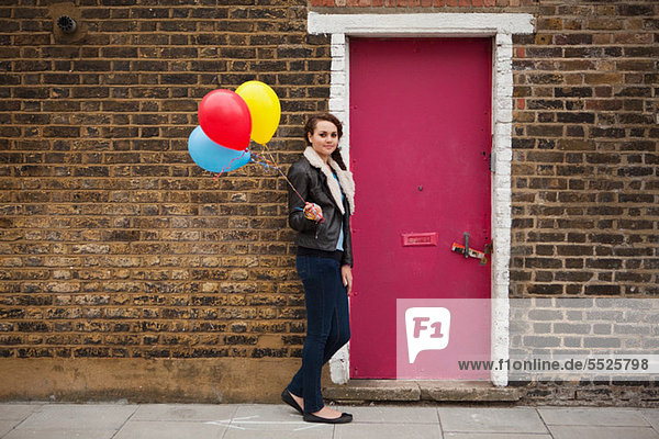 Young Woman holding bunten Luftballons gegen Wand