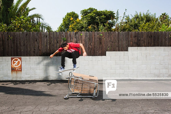Mann über Skateboard springen kaufen Einkaufswagen