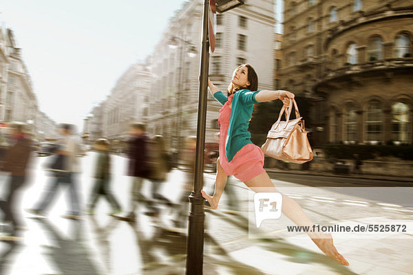 Mittlere erwachsene Frau in rosa Kleid  die durch die Straßen der Stadt springt.