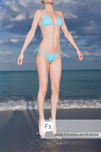 Frau mittleren Alters im Bikini am Strand Tigersprung
