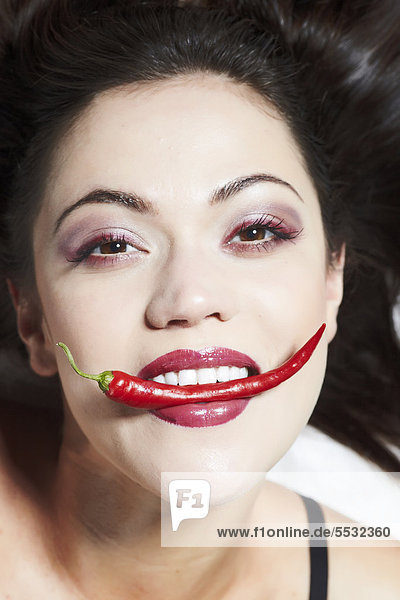Portrait einer jungen Frau mit Peperoni zwischen den Zähnen mund