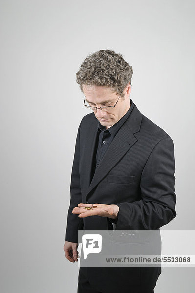 Businessman wearing a black suit gloomily looking at the few coins in his hand
