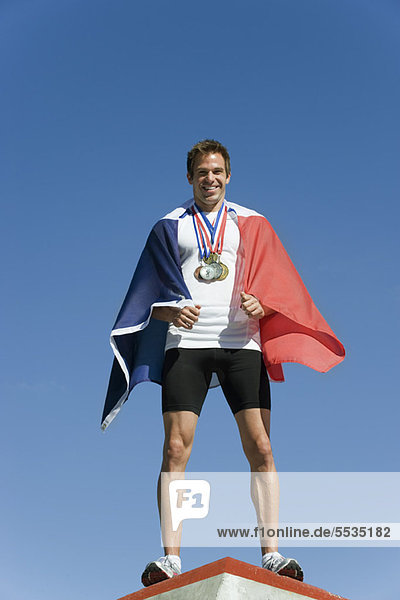 Männlicher Athlet wird auf dem Podium geehrt  in französische Flagge gehüllt