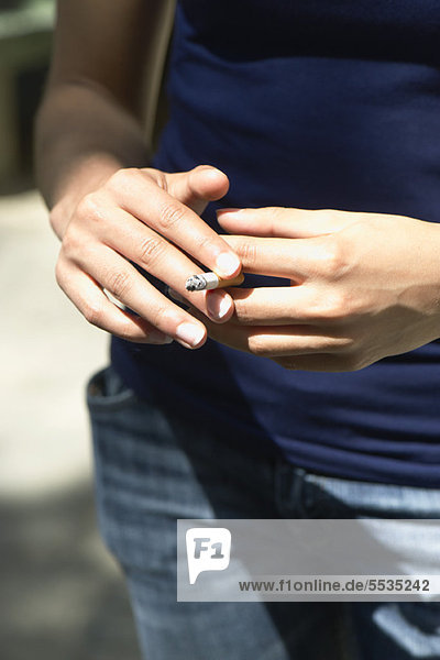 Woman holding lit cigarette  cropped