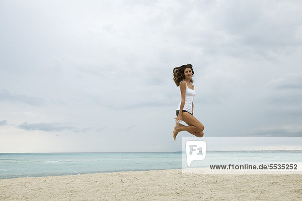 Junge Frau beim Luftspringen am Strand