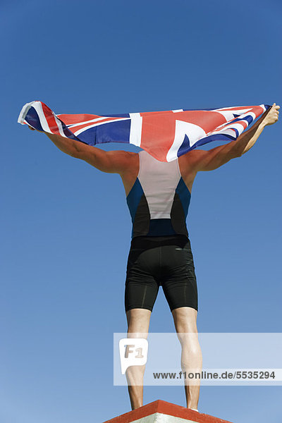 Männlicher Athlet auf dem Podium  hält die britische Flagge hoch  Rückansicht