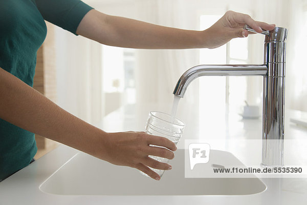 Woman filling glass of water at kitchen sink  cropped