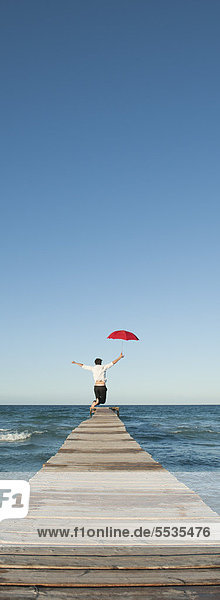 Mann springt auf Pier mit Schirm  Rückansicht