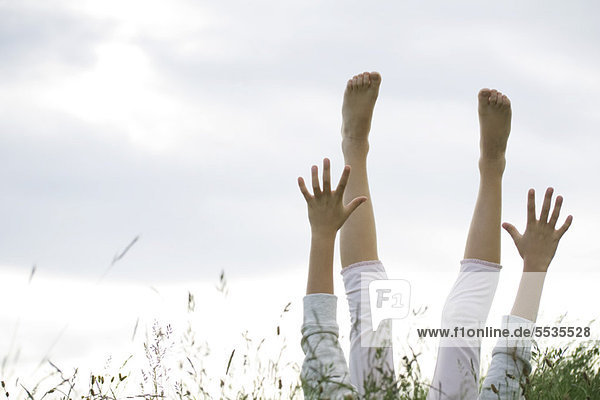 Mädchen auf dem Rücken liegend im hohen Gras mit erhobenen Armen und Beinen
