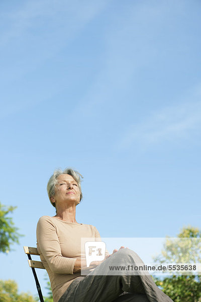 Senior woman sitting outdoors enjoying warmth of sun